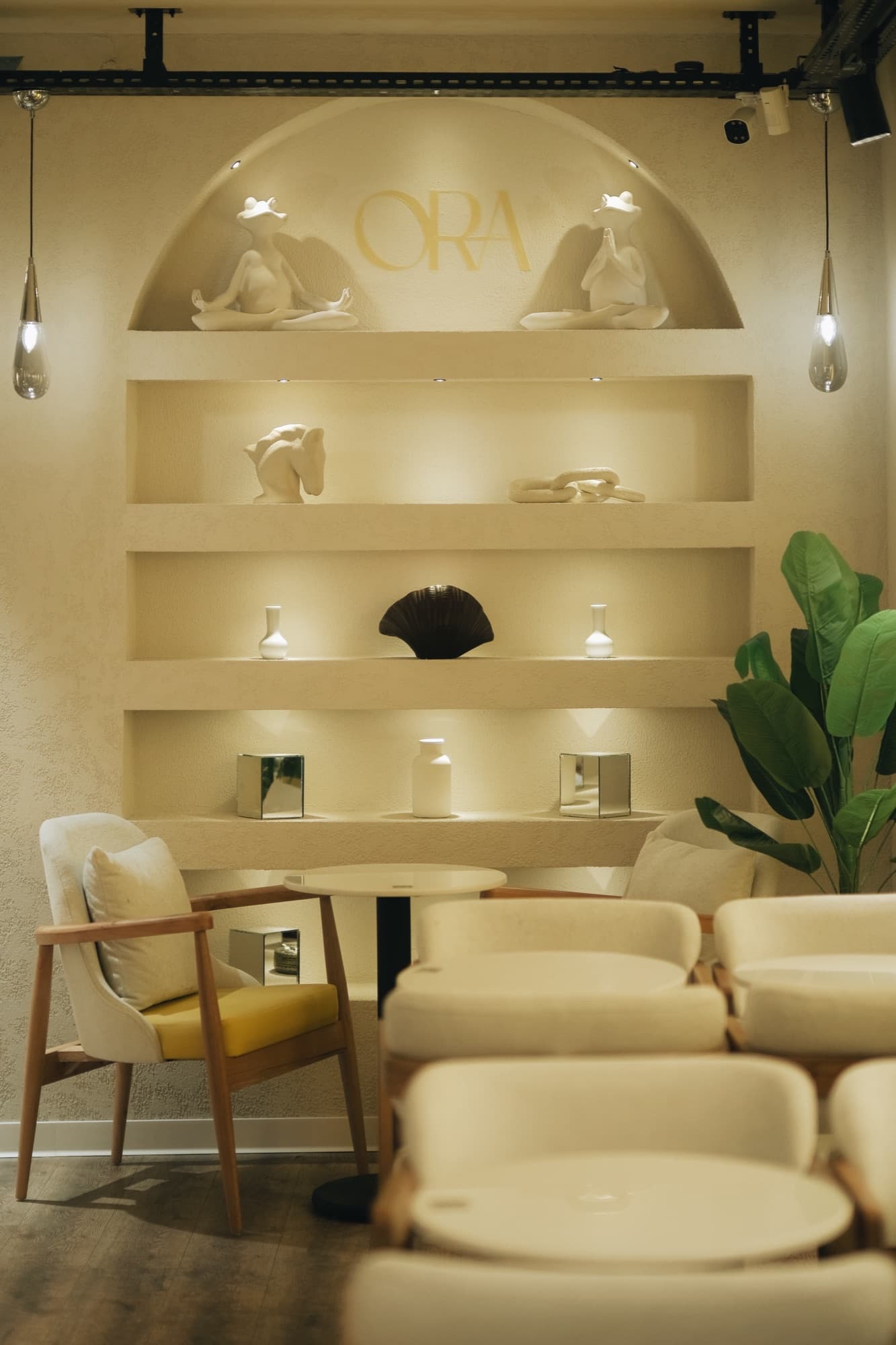 ORA Coffee'nin iç mekânı: kemerli nişte altın ORA yazısı, krem sıvalı raflar, bukle koltuklar ve sarı minderli sandalye.