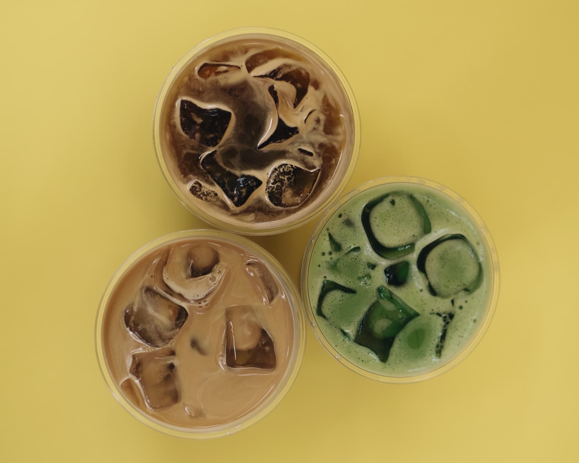 Sarı zeminde üstten çekilmiş üç buzlu içecek: cold brew, iced latte ve iced matcha.